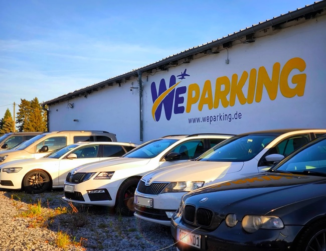 Zbliżenie na zaparkowane samochody przed budynkiem WE Parking z dużym logotypem na fasadzie.