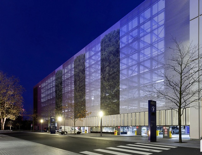 Parking Mein-Flughafenparkplatz-Frankfurt ShortWay - se puede ver un moderno edificio de estacionamiento. Al lado crecen árboles y hay un cartel informativo.