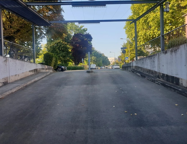 Rampa prowadząca w górę z podziemnego parkingu na powierzchnię, otoczona zielenią i drzewami.