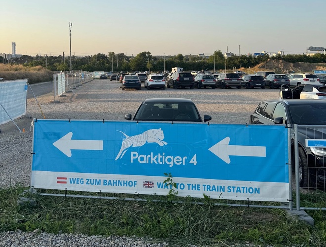 Niebieski baner ukazujący białą strzałkę, wskazującą kierunek do stacji pociągów w celu dotarcia na lotnisko z parkingu.