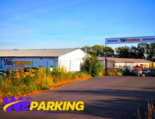 Widok na budynek WE Parking z zewnątrz, otoczony zaparkowanymi samochodami i zielenią.