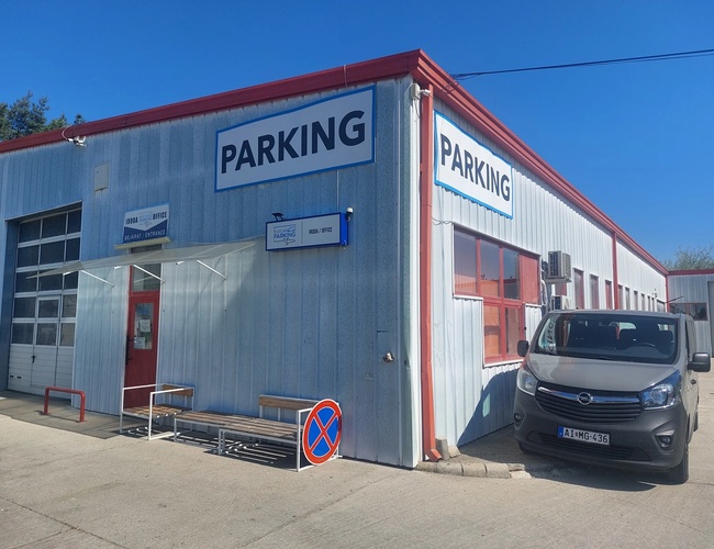 Parking BUDCAR - Widać zaparkowany bus przy budynku. Na budynku jest widoczny plakat reklamowy z nazwą parkingu.