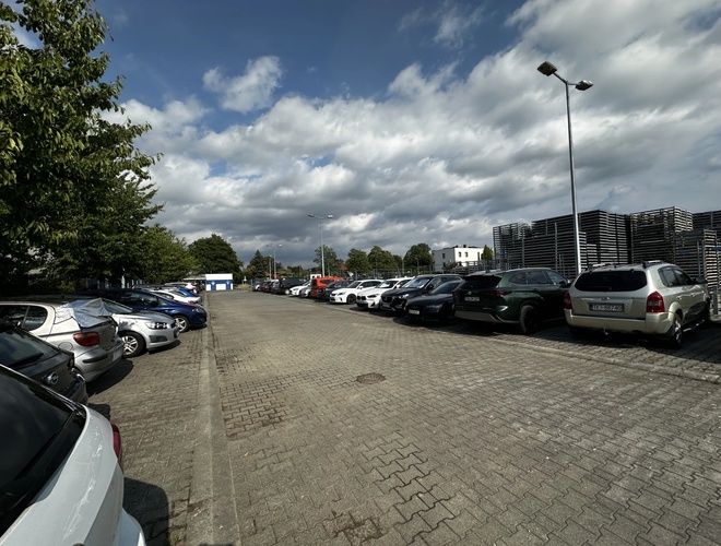 Widok samochodów zaparkowanych na parkingu, który jest w pełni wyłożony kostką brukową.