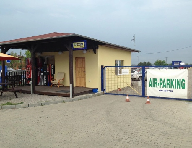 Budynek biura obsługi parkingu lotniskowego z napisem 'AIR-PARKING', otoczony ogrodzeniem i utwardzonym placem.