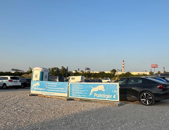 Widok parkingu z wieloma zaparkowanymi pojazdami. Na ogrodzeniu widoczne kolejne banery z nazwą parkingu.