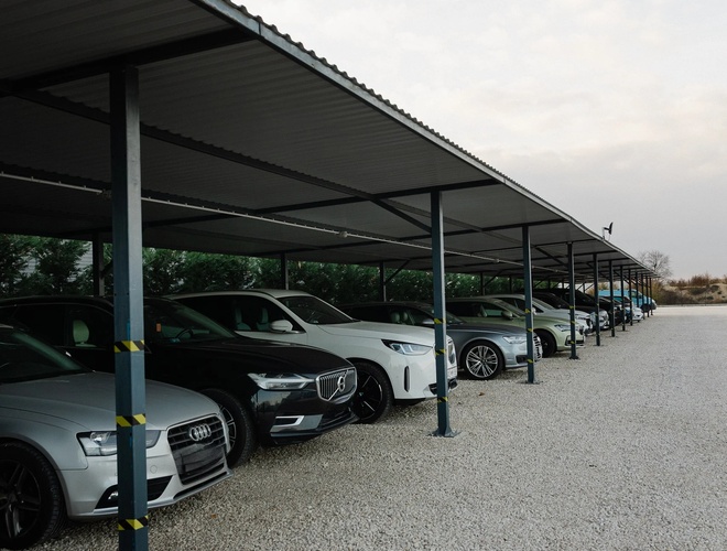 Zadaszony parking długoterminowy z rzędami samochodów osobowych zaparkowanych pod metalową wiatą