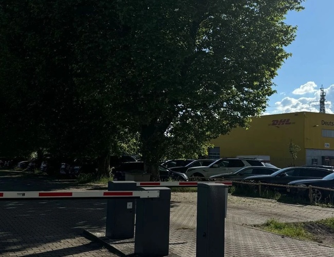 Parking Park & Go Valet – widoczny szlaban wjazdowy na parking. W tle drzewa i samochody.