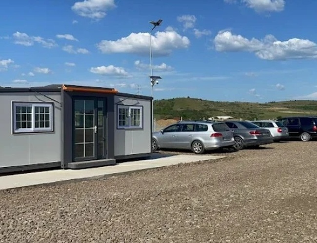 Kontener biurowy na placu z zaparkowanymi samochodami, pod niebem z lekkim zachmurzeniem