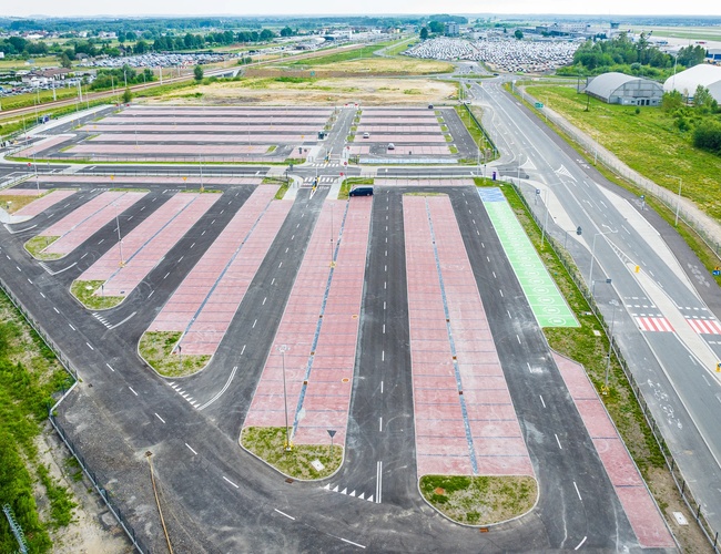 Widok z lotu ptaka na duży, pusty parking z wyznaczonymi miejscami postojowymi i drogami dojazdowymi.