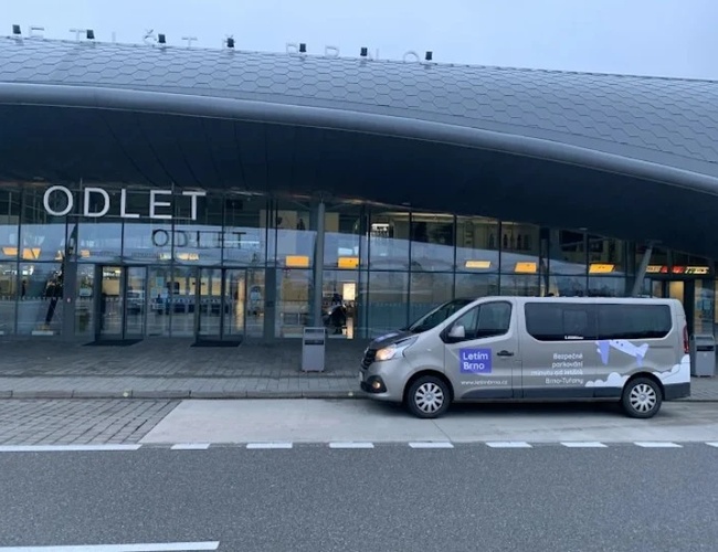 Parking Letim Brno II – na terenie odlotów stoi zaparkowany bus transferowy z oznaczeniem na boku wskazującym nazwę parkingu. W tle teren lotniska oraz widoczna strefa odlotów.
