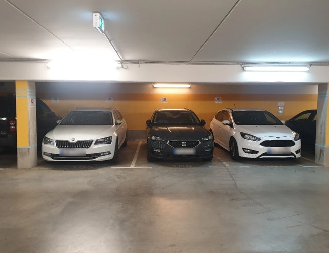 Trzy zaparkowane samochody na podziemnym parkingu, żółta ściana i sufit z oświetleniem LED.