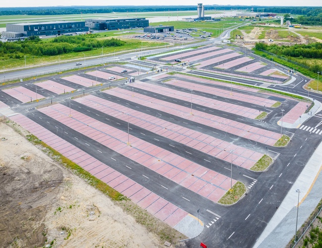 Widok z góry na pusty parking z białymi liniami miejsc postojowych i pasami jezdni. Szara, płaska nawierzchnia, w tle mogą być latarnie i znaki drogowe.