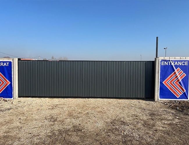 Wejście na parking ogrodzone ciemnym metalowym płotem, po bokach tablice informacyjne z oznaczeniem ‘Entrance’.