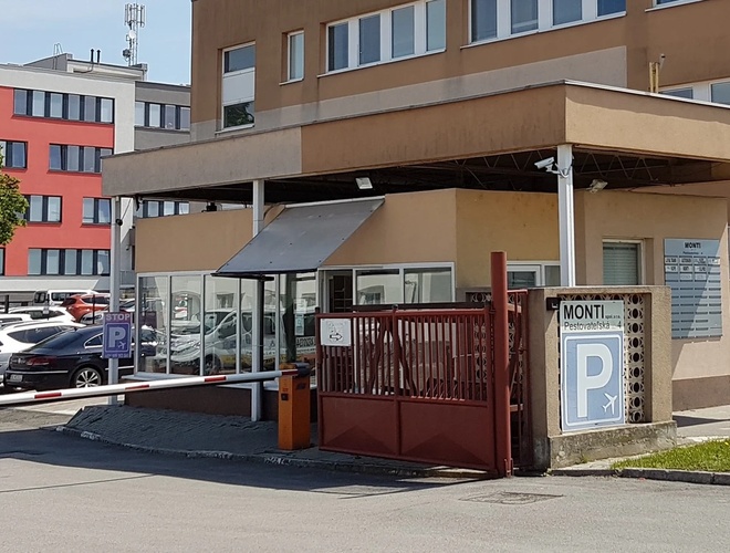 Budynek z wjazdem na parking, ogrodzony, z kilkoma samochodami zaparkowanymi przed wejściem.