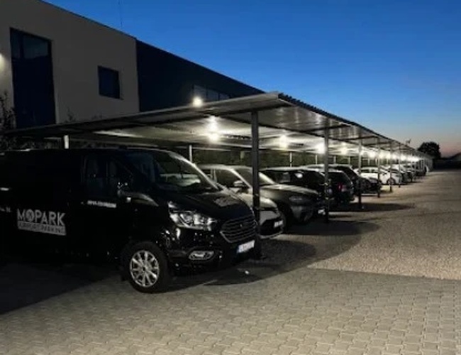 Zadaszony parking lotniskowy po zmroku z oświetlonymi miejscami postojowymi i zaparkowanymi autami