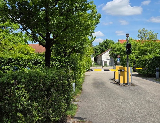 Szlaban pokazujący wjazd na teren parkingu, wokoło zieleń i drzewa