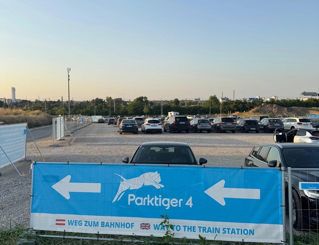 Niebieski baner ukazujący białą strzałkę, wskazującą kierunek do stacji pociągów w celu dotarcia na lotnisko z parkingu.