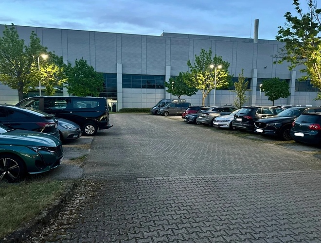 Auta zaparkowane na parkingu z kostki brukowej, dookoła drzewa i latarnie