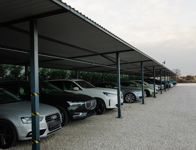 Zadaszony parking długoterminowy z rzędami samochodów osobowych zaparkowanych pod metalową wiatą
