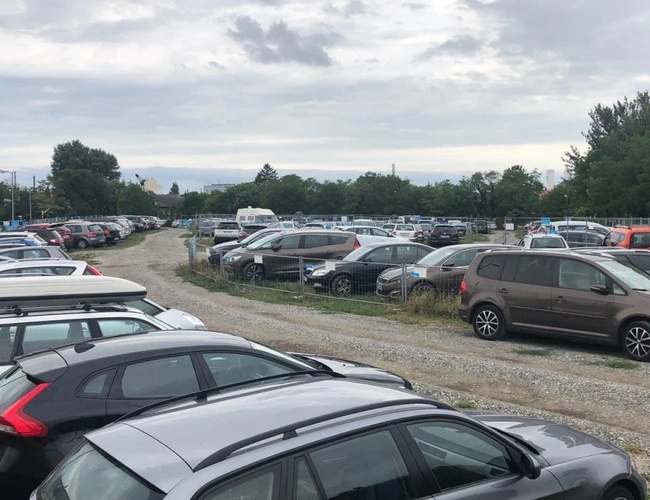 Parktiger Airport Parking 4 - Duży, nieutwardzony parking z licznymi samochodami. Teren jest otwarty i oświetlony. Widoczne są drzewa w tle.