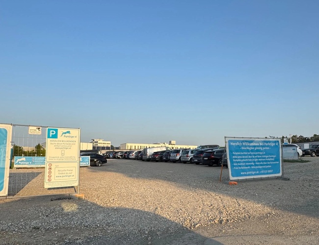 Widoczny teren parkingu z kilkoma znakami informacyjnymi oraz zaparkowanymi samochodami.