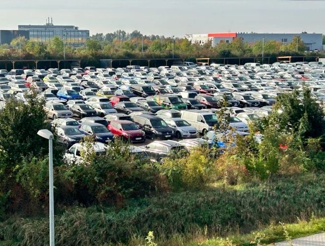 Parcare P365 - O parcare mare plină de mașini. Zona este înconjurată de vegetație și garduri. Apare lumina felinarelor în spațiu.