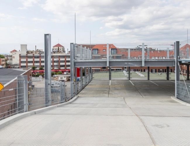 Parking Best Valet Park Service – betonowe miejsca parkingowe na piętrowym parkingu odkrytym. W tle budynki, niebo z chmurami.
