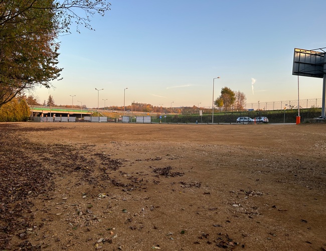 Victory Cars – parking no pavimentado, cercado, con farolas visibles. Al fondo, algunos árboles y una valla.