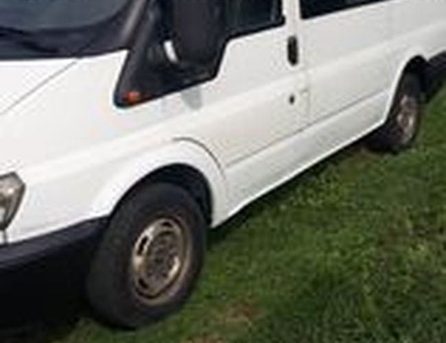 Parking Park&Fly – biały van stoi na zielonej trawie. Obok widać fragment budynku. Van jest zwrócony przodem w lewo.