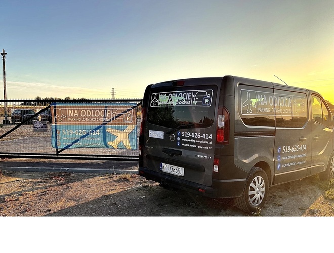 Aparcamiento en Salidas – puerta de metal con un cartel informativo. Al lado hay una furgoneta oscura con un anuncio de aparcamiento.