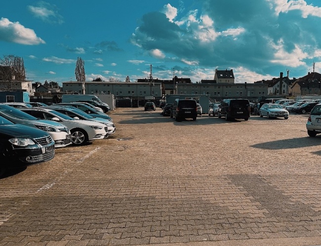 Bezpečnosť parkovania parking24 VALET – Parkovisko zaplnené autami v rade. Priestor je rovný a otvorený. Na obzore sú viditeľné budovy.