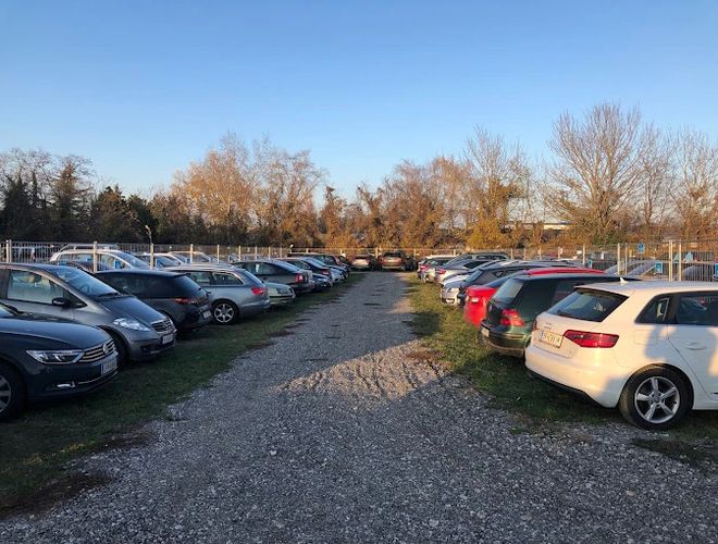 Parking Parktiger Transfer - Auf dem Bild ist ein großer Parkplatz zu sehen, der mit Autos gefüllt ist. Der Parkplatz ist eingezäunt und hat eine Kiesoberfläche.