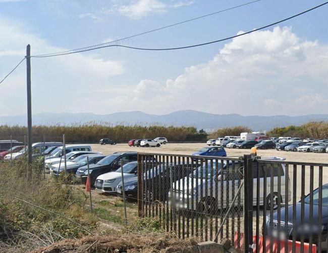 Central Parking Valet - Parking jest ogrodzony i pełen samochodów. Brama jest otwarta. Teren jest nieutwardzony, a w tle widać góry.
