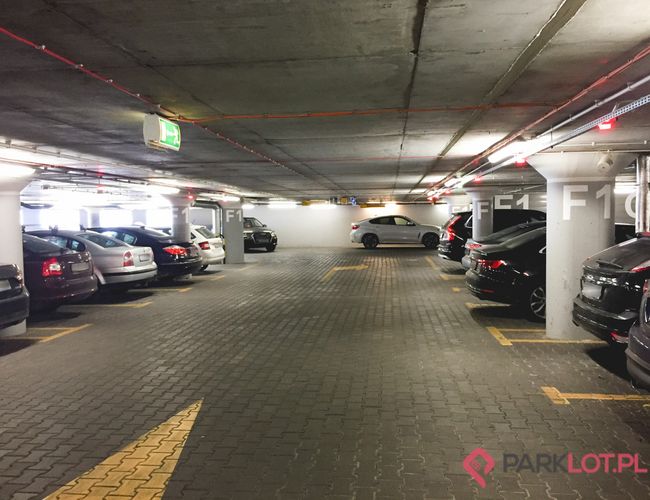 Oficjalny Parking Lotniska P2 – parking podziemny, wiele samochodów, dobre oświetlenie. Widoczna jest wyraźnie oznaczona droga ewakuacyjna.