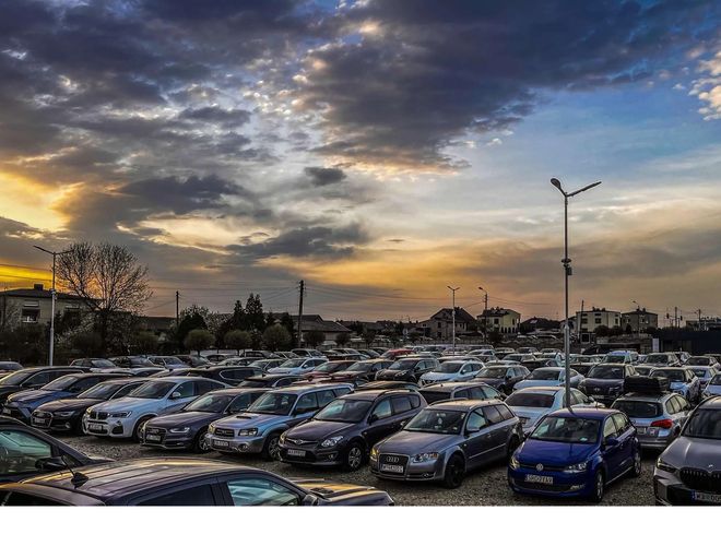 GoPark – Parking jest zapełniony samochodami. Teren jest oświetlony latarniami. W tle widać budynki.