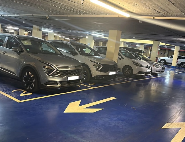 Parkovanie auta a Fly Garage Valet – Podzemná garáž s autami. Miesta sú označené modrou farbou. Jasné osvetlenie pod stropom.