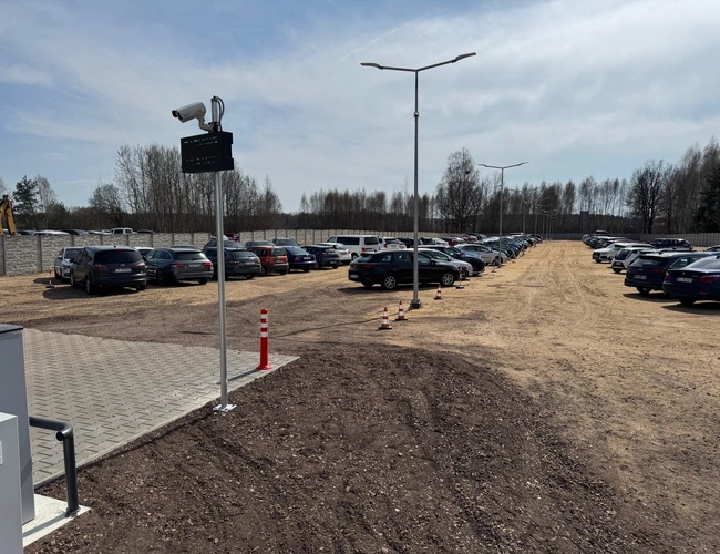 SkyParking - El aparcamiento está cercado y iluminado. En el recinto hay coches. Una cámara monitorea el área.