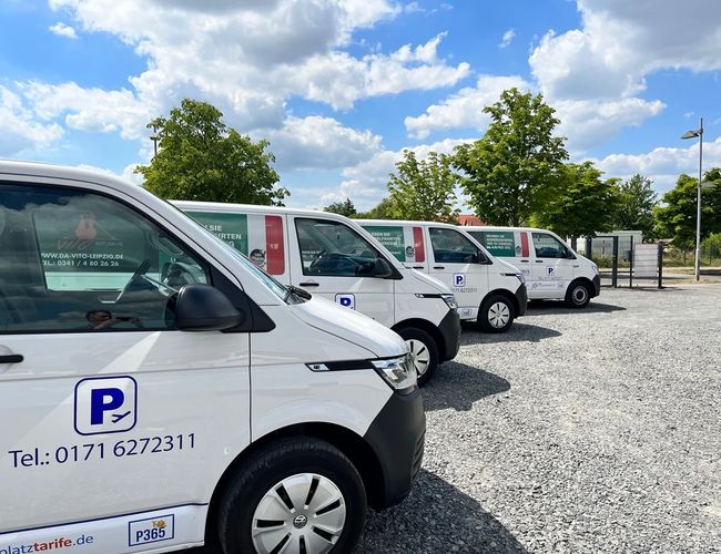 Parkering P365 – Flere hvite busser står ved siden av hverandre. Området er gruslagt og omgitt av trær.