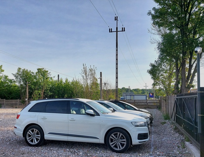 Parkovisko MPark – niekoľko áut zaparkovaných na škvárovej ploche. Povrch je ohradený kovovým plotom. V pozadí sú vidieť stromy a obloha.