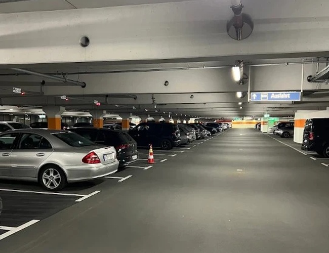 Hala parkingowa z rzędami zaparkowanych samochodów i oświetleniem sufitowym.