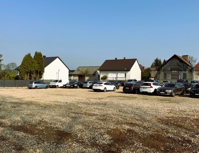 Parkovanie Amber – Na štrkovom námestí stojí mnoho áut. V pozadí vidieť domy a stromy.