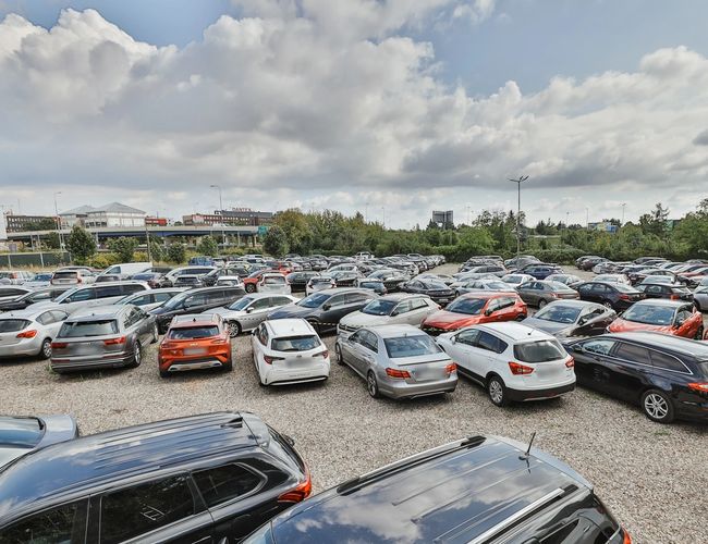 Smart Supreme Parking - Duży, zapełniony parking z wieloma autami. Teren jest otwarty i nieogrodzony. Na niebie widoczne są chmury.