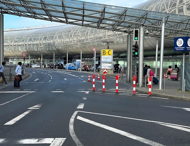 Parking Marspark Outdoor Valet - ruchliwy obszar przed terminalem lotniska. Widoczny zadaszony chodnik z barierkami. Znaki wskazują kierunki poruszania się.