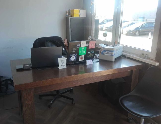 Aparcamiento en el 5 - oficina con vista al aparcamiento. En el escritorio hay una laptop y una carpeta. Por la ventana se ven los coches aparcados.