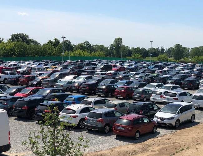 Smart Premium Parking - Parking pełen samochodów osobowych. Obszar jest ogrodzony i otoczony zielenią. Znajdują się tu latarnie.
