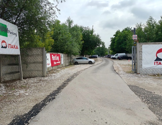 WAW Parking – Teren pietruit cu adăpost și container. Lângă cresc copaci și sunt parcate mașini. Vremea este însorită.