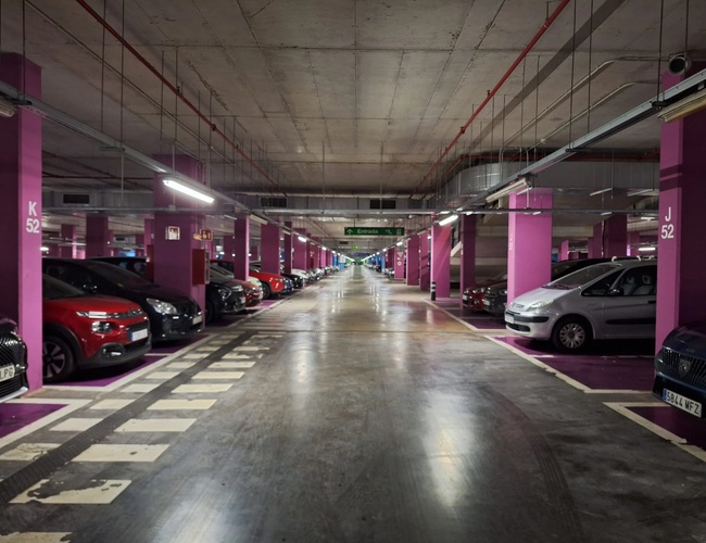 Parkovanie Low Valet - Viditeľné zastrešené podzemné parkovisko. Rada zaparkovaných áut po oboch stranách. Jasné osvetlenie vytvára priateľskú atmosféru.