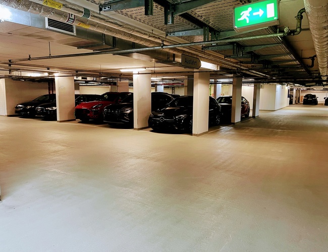 Royal Valet Parking – Podzemné parkovisko s autami a označením výstupu. Je dobre osvetlené. Vidno niekoľko áut zaparkovaných vedľa seba.