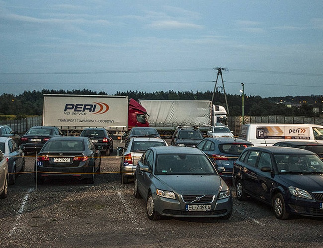 PERI Parking - En el aparcamiento hay coches y un camión estacionados. El área está cercada y iluminada con farolas.