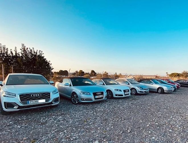 Der beste Parkplatz Alicante Außen-Parkservice – Einige Autos stehen auf terrassenartigem Gelände. Im Hintergrund sind eine Zaunanlage und Bäume zu sehen.